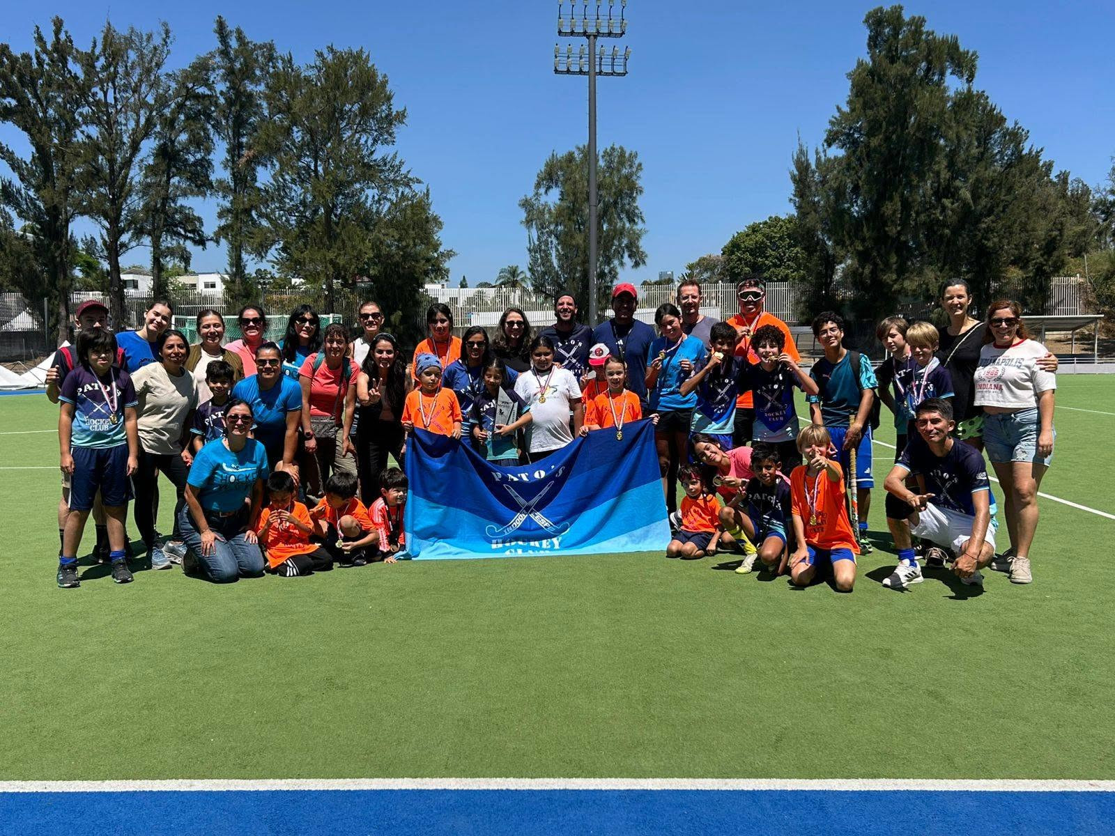 Niñas y niños jugando hockey en césped sintético con sus coaches